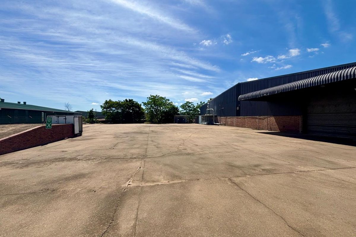 A spacious commercial concrete yard featuring a large warehouse building with a covered loading bay and brick retaining wall.