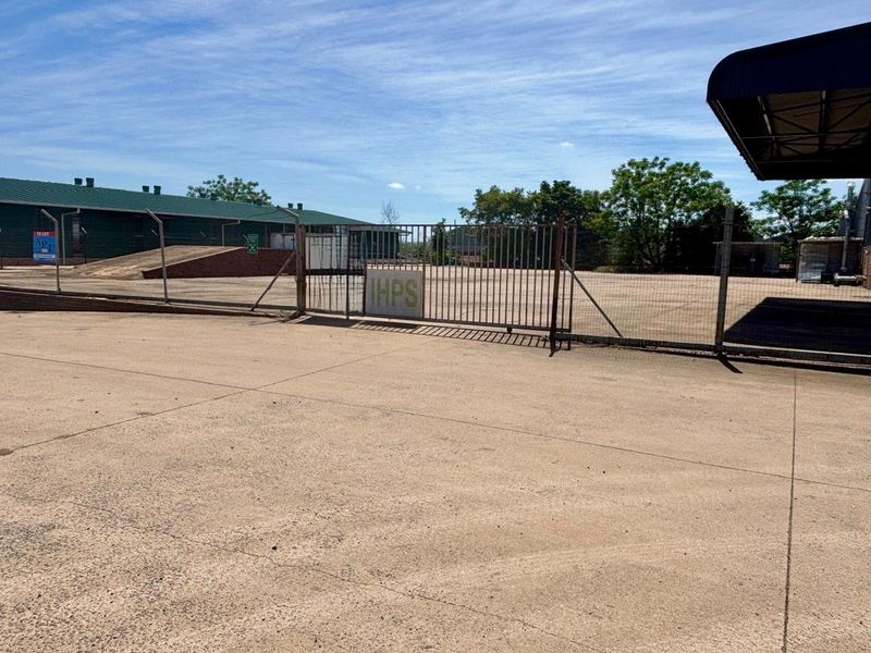 A commercial vacant land area featuring concrete paving, secure metal fencing, a gated entrance, and a loading ramp.