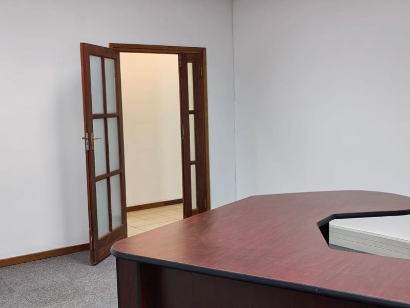 A functional office space featuring carpeted flooring and double glass-panelled doors leading to an adjacent room.