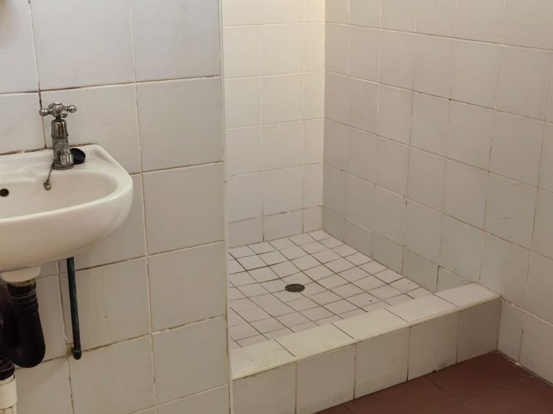 A functional bathroom featuring a wall-mounted basin with exposed plumbing and a tiled shower enclosure with a raised threshold.
