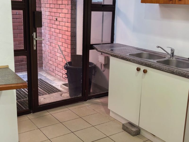 A functional kitchen area featuring a double bowl sink, laminate countertops, and built-in cabinetry with direct access to an exterior courtyard.
