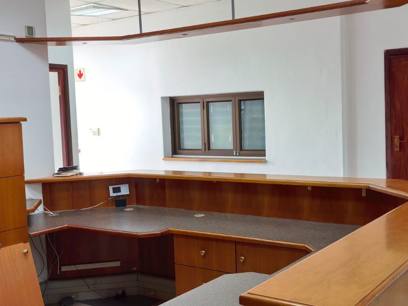 A vacant commercial office space featuring a large built-in reception desk, tiled flooring, and timber doors, suitable for a professional workspace.