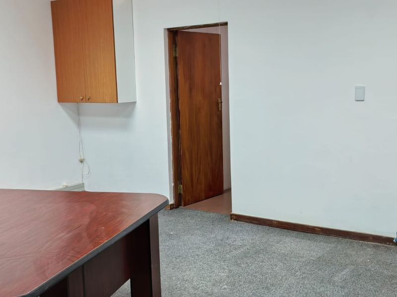 A functional office space featuring built-in wall cabinetry, carpeted flooring, and a timber door, providing a practical workspace environment.