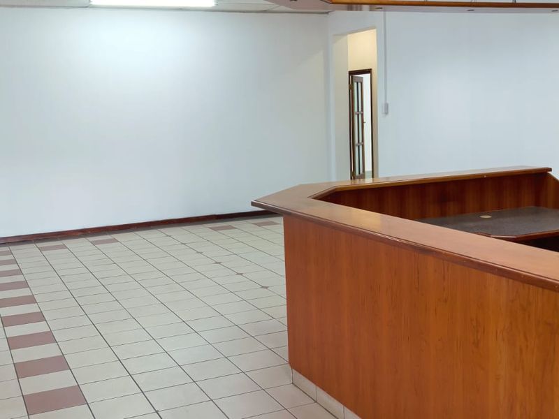 An open-plan commercial office space featuring a built-in wooden reception desk, tiled flooring, and neutral walls, suitable for a professional workspace.