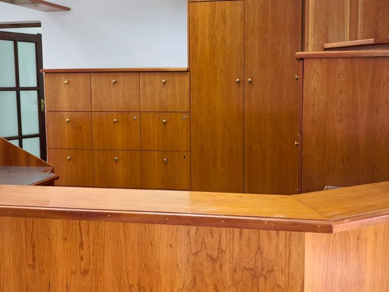 A professional office space featuring extensive built-in wooden cabinetry and a functional reception desk, providing ample storage and a clean, organized workspace.