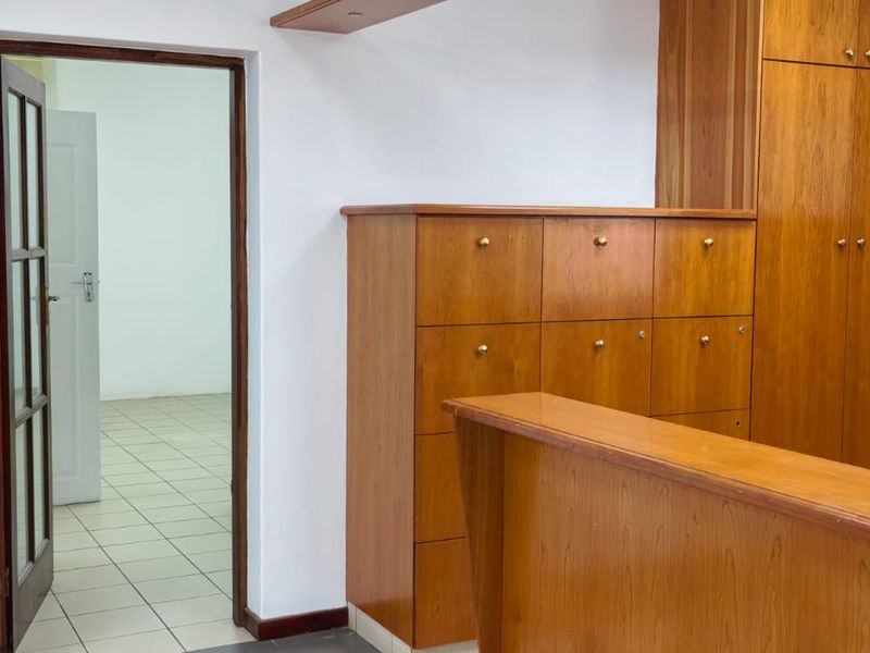 Commercial office space featuring extensive built-in wooden cabinetry, a reception counter, and tiled flooring, leading into an adjacent room through a timber-framed doorway.