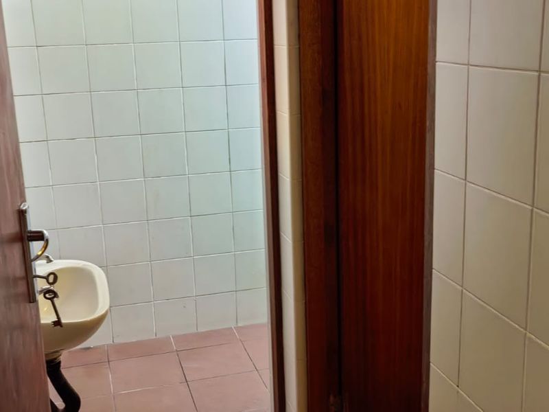 A small, dated bathroom featuring white wall tiles, terracotta floor tiles, and a pedestal sink, requiring cosmetic updates to improve its overall condition.