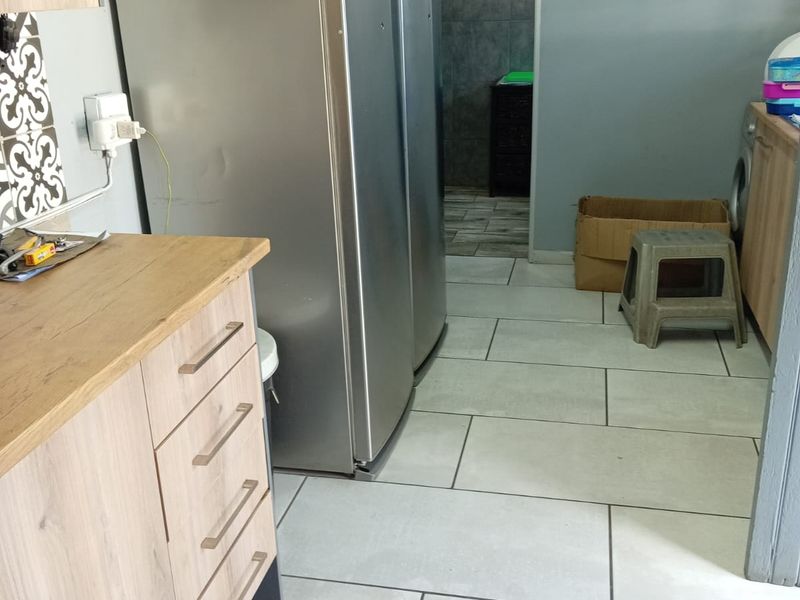 A functional utility space featuring light wood-finish cabinetry, large format floor tiles, and a doorway leading to an adjacent tiled area.