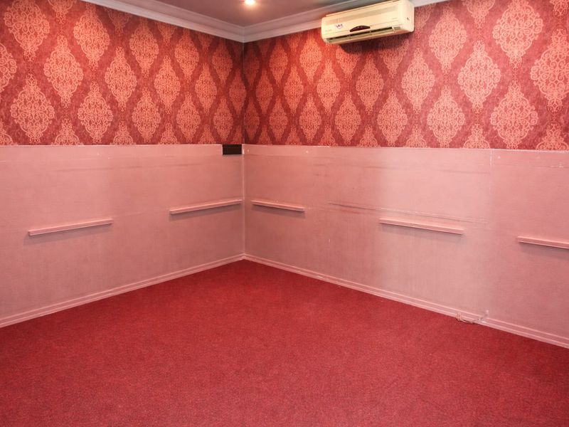 An empty commercial room featuring red patterned wallpaper, lower wall paneling, fitted wall shelves, and a wall-mounted air conditioning unit.
