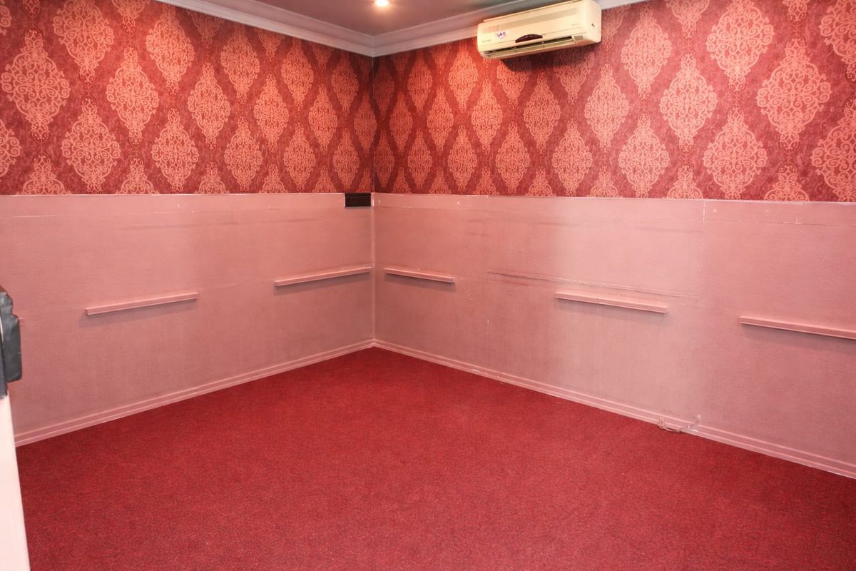 An empty commercial room featuring red patterned wallpaper, lower wall paneling, fitted wall shelves, and a wall-mounted air conditioning unit.