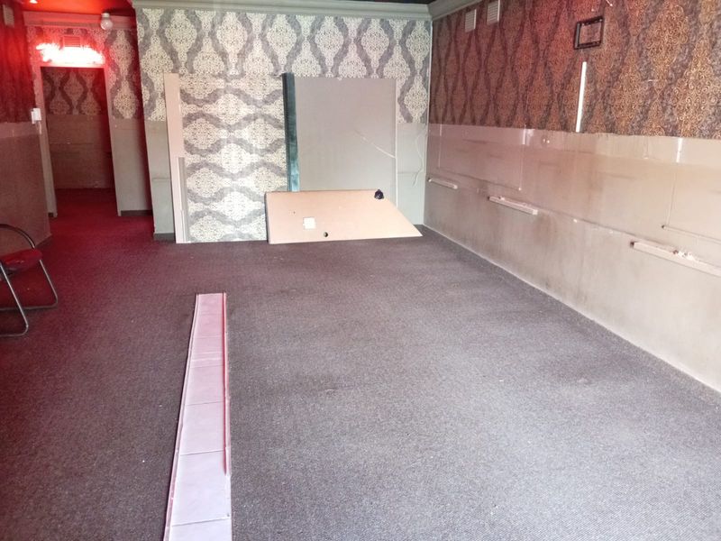 An empty commercial interior space featuring patterned wallpaper, carpeted flooring, and visible wall fixtures, currently in need of renovation and repair.