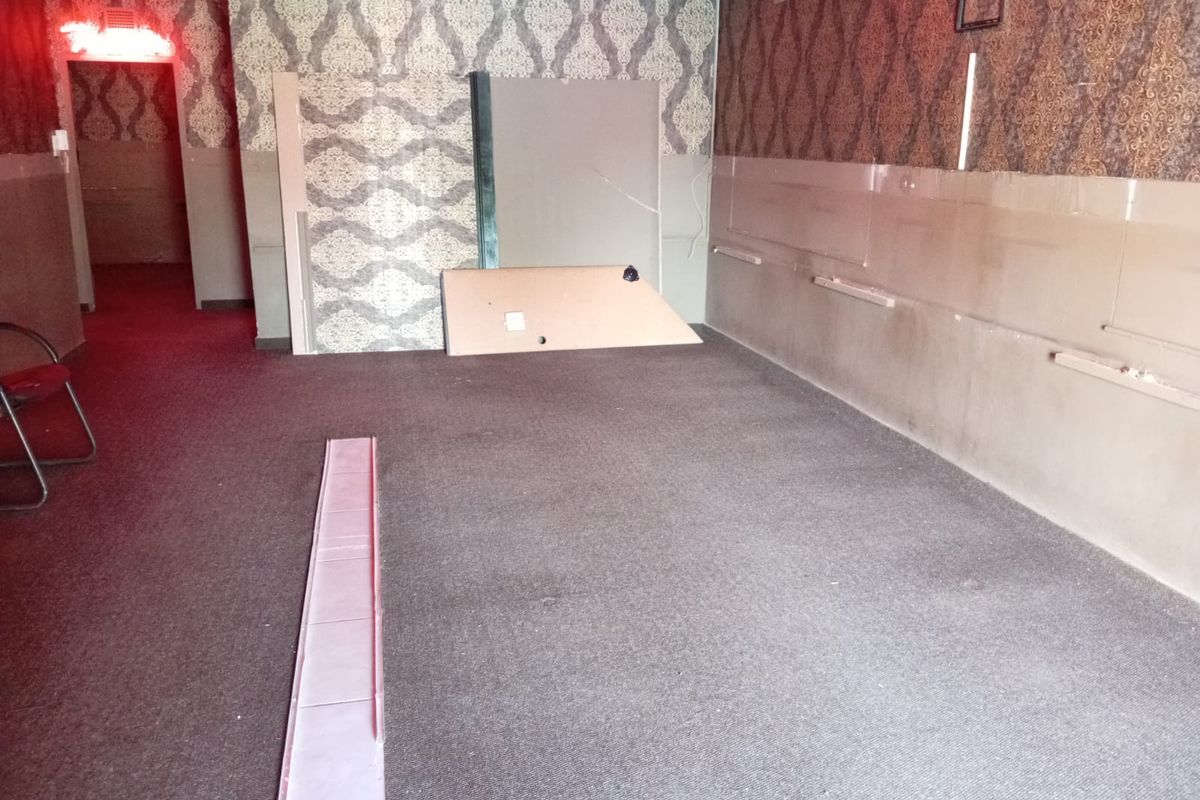 An empty commercial interior space featuring patterned wallpaper, carpeted flooring, and visible wall fixtures, currently in need of renovation and repair.