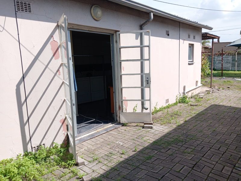 Exterior view of a commercial building rear entrance featuring paved area, double metal doors, and visible signs of exterior wall maintenance required.