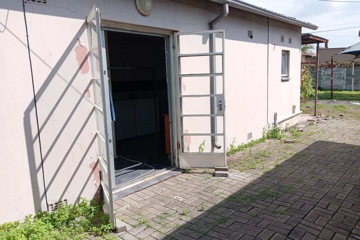 Exterior view of a commercial building rear entrance featuring paved area, double metal doors, and visible signs of exterior wall maintenance required.