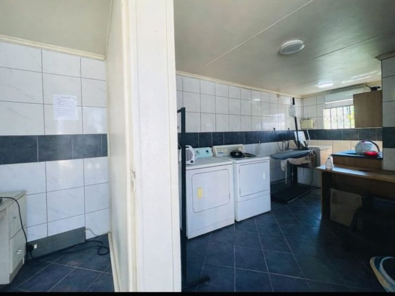 A functional laundry room featuring tiled walls, dark floor tiling, and dedicated space for washing and drying appliances.