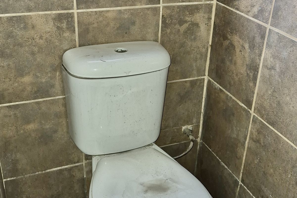 A compact bathroom featuring tiled walls and flooring with a standard toilet fixture situated beneath a window.