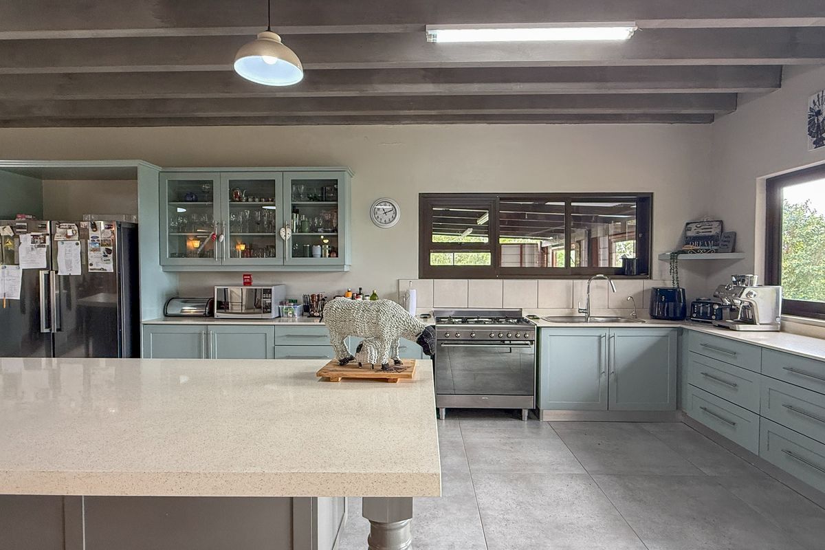 Spacious farmhouse kitchen featuring a large central island, quartz countertops, light blue cabinetry, gas stove, and exposed ceiling beams with tiled flooring.