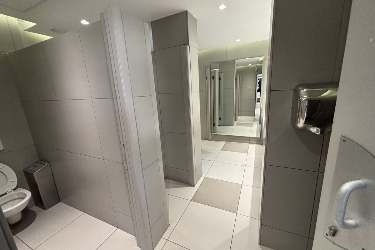 Modern commercial bathroom facility featuring tiled walls and flooring, partitioned cubicles, recessed lighting, and a wall-mounted hand dryer.
