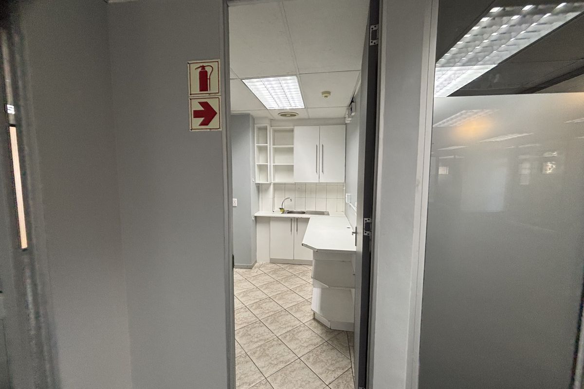 A compact office kitchenette featuring built-in cabinetry, a stainless steel sink, tiled flooring, and functional drop ceiling lighting.