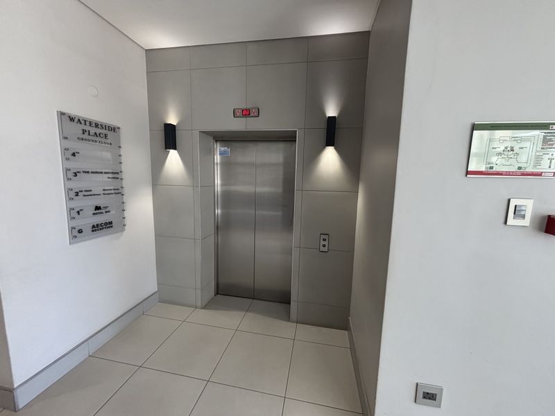 Modern office building lobby entrance featuring a stainless steel elevator, tiled flooring, and professional directory signage.