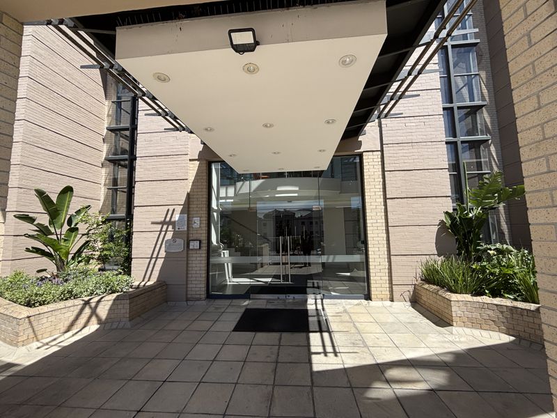 Modern office building entrance featuring a covered canopy, glass doors, and well-maintained brick facade with integrated planters.