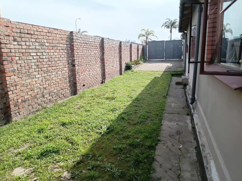 A side yard area featuring a long brick boundary wall, a concrete walkway, and a gated access point to the rear of the property.