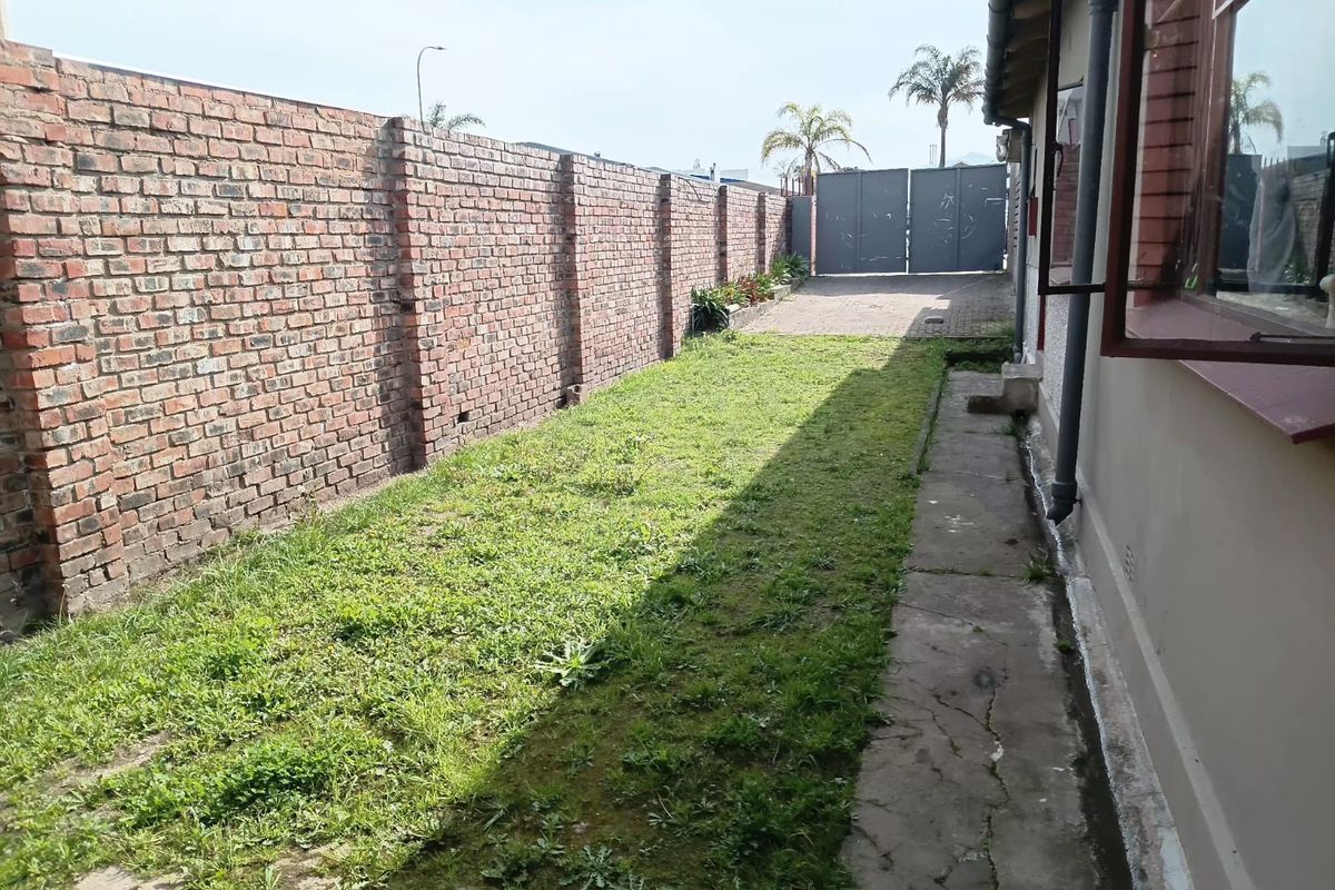 A side yard area featuring a long brick boundary wall, a concrete walkway, and a gated access point to the rear of the property.