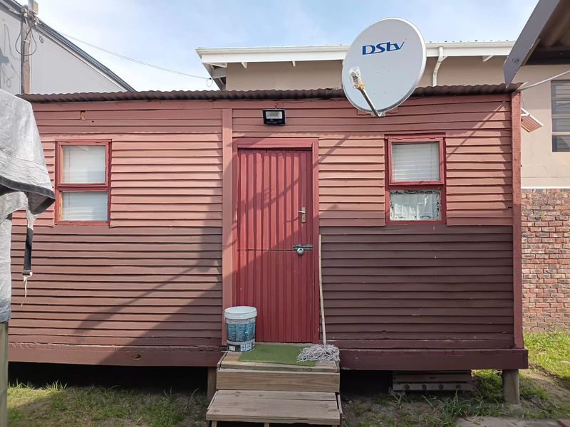 Exterior view of a timber-clad structure featuring a corrugated metal roof, satellite dish, and wooden entrance steps.