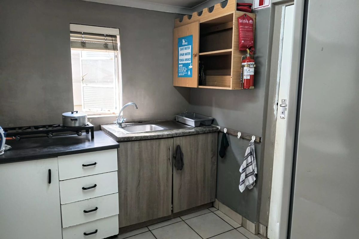 A compact kitchen area featuring built-in cabinetry, a stainless steel sink, laminate countertops, and tiled flooring, equipped with essential fire safety equipment.