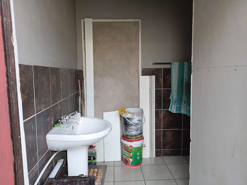 A small bathroom space featuring a pedestal basin and partial wall tiling, currently in an unfinished state requiring renovation and completion of wall finishes.