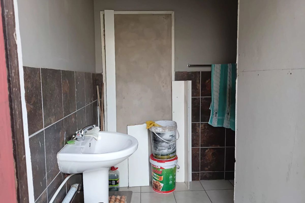 A small bathroom space featuring a pedestal basin and partial wall tiling, currently in an unfinished state requiring renovation and completion of wall finishes.
