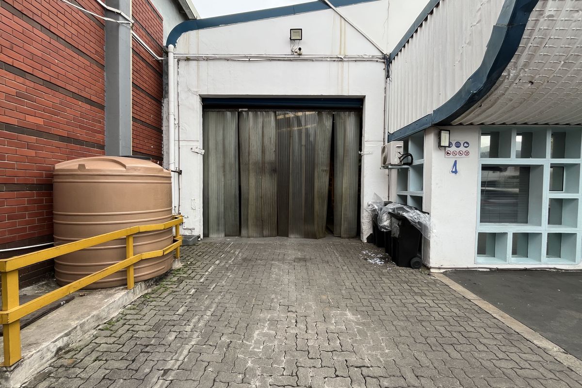 Industrial exterior view featuring a large roller shutter access point, paved driveway, and external water storage tank.