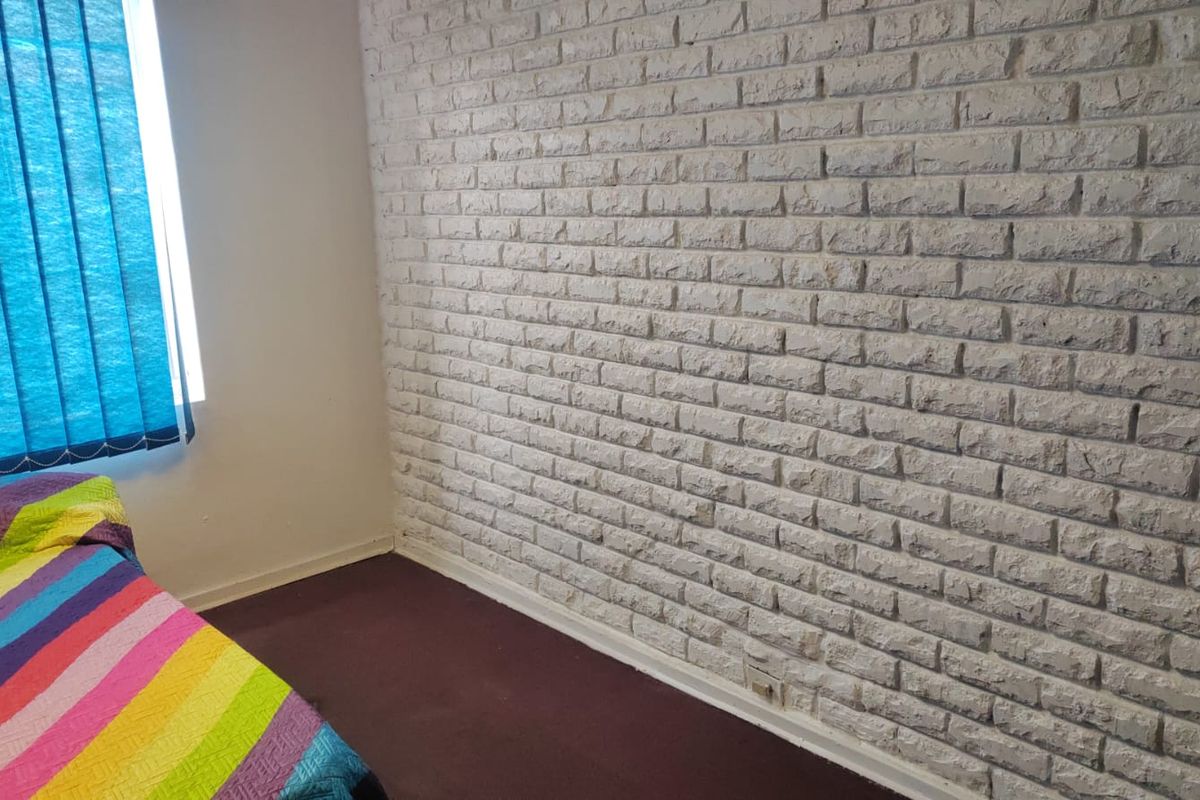 A bedroom featuring a textured white brick feature wall, dark carpeting, and a window with blue vertical blinds.