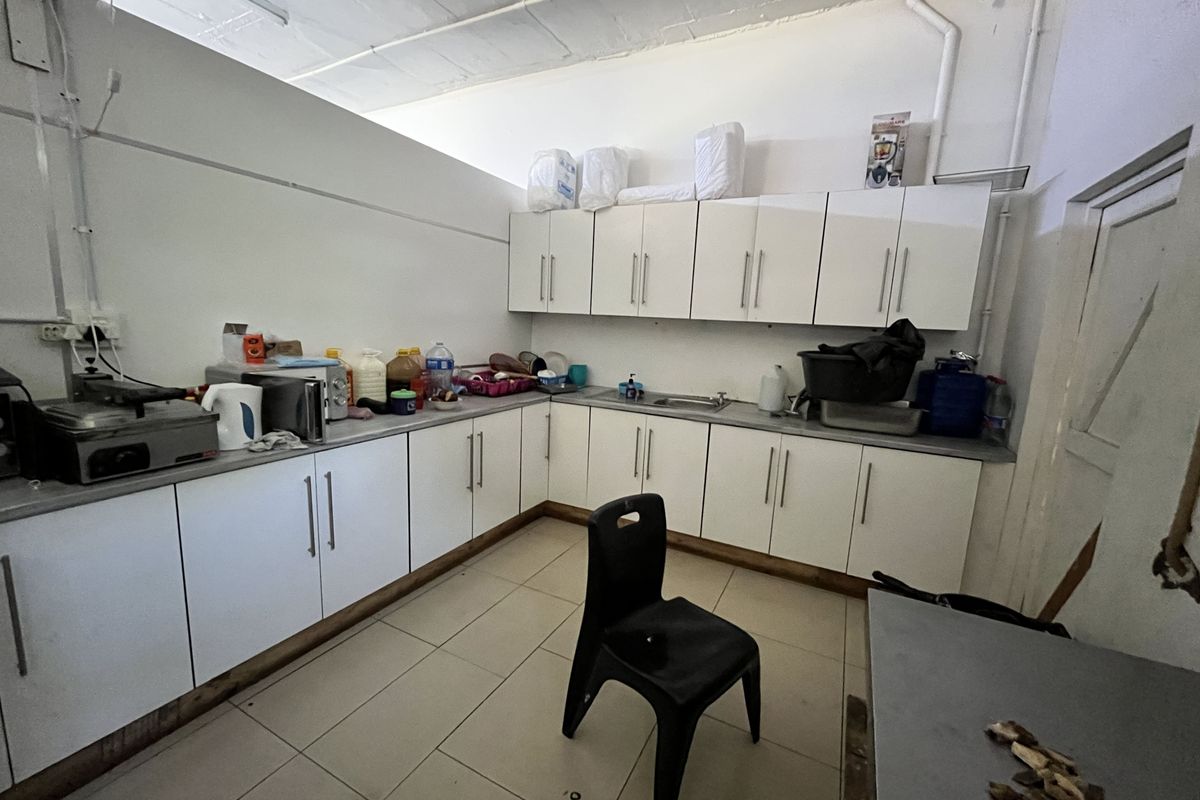 A functional kitchenette area featuring white cabinetry, tiled flooring, and exposed ceiling structure, suitable for office staff use.
