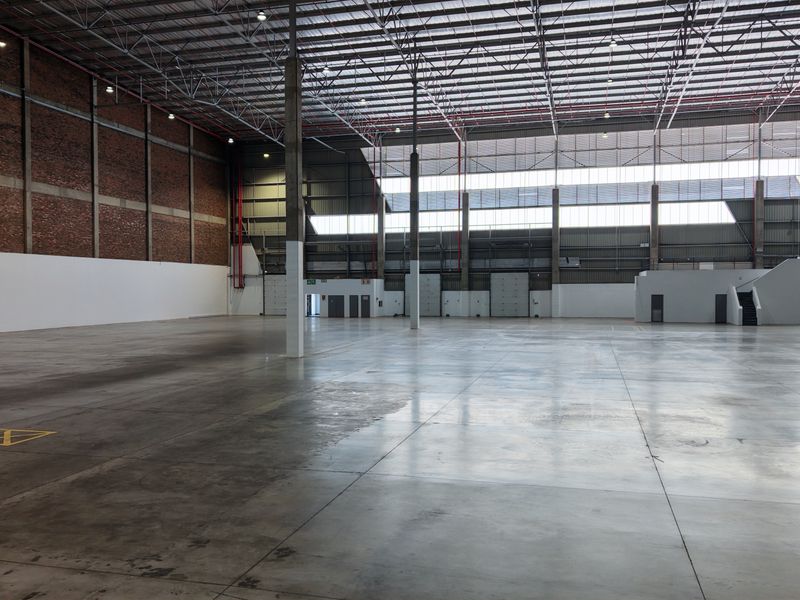 Expansive industrial warehouse space featuring high ceilings, exposed steel trusses, durable concrete flooring, and multiple roller shutter access points.