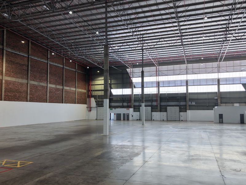 Spacious industrial warehouse featuring high ceilings with exposed steel trusses, polished concrete flooring, brick wall accents, and integrated fire sprinkler systems.