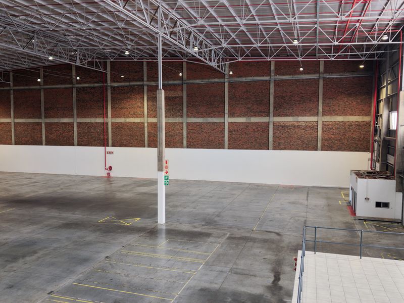 Spacious industrial warehouse featuring high ceilings with exposed steel trusses, durable concrete flooring, and brick wall finishes, suitable for various commercial or storage operations.
