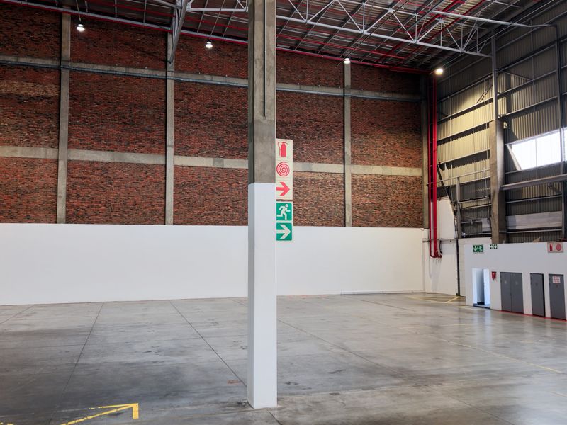 Spacious industrial warehouse unit featuring high ceilings, exposed brickwork, concrete flooring, and integrated fire safety systems, suitable for various commercial or storage operations.