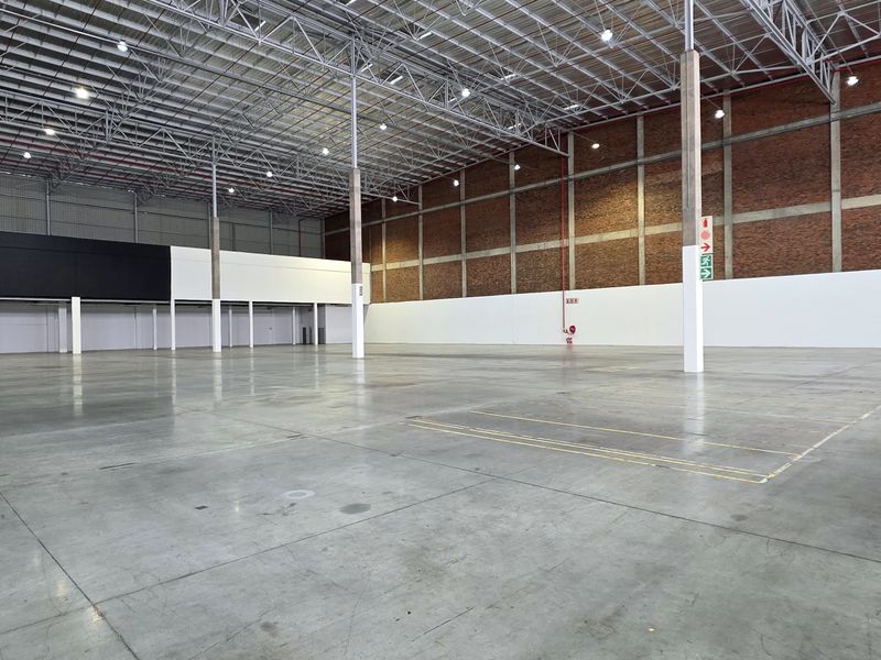 Spacious industrial warehouse featuring high ceilings with exposed steel trusses, polished concrete flooring, and durable brick wall finishes.