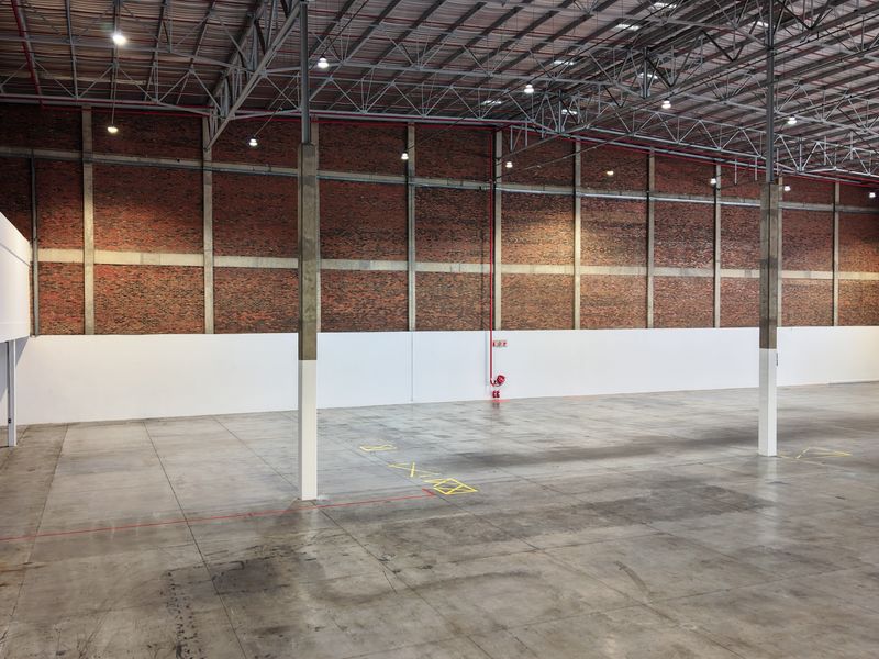 Spacious industrial warehouse featuring high ceilings with exposed steel trusses, concrete flooring, and brick wall detailing, suitable for storage or manufacturing operations.