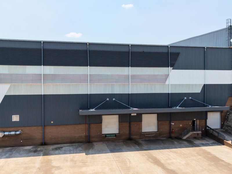 Aerial view of an industrial warehouse exterior featuring multiple loading docks, roller shutter doors, and a spacious concrete yard for logistics operations.