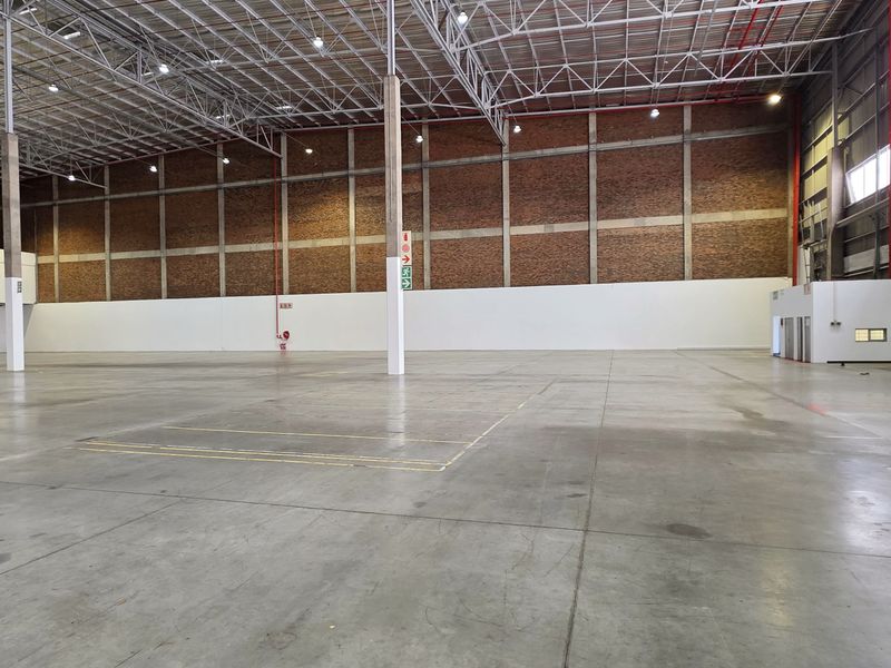 Spacious industrial warehouse featuring high ceilings with exposed steel trusses, durable concrete flooring, and brick walling, suitable for various commercial or storage operations.