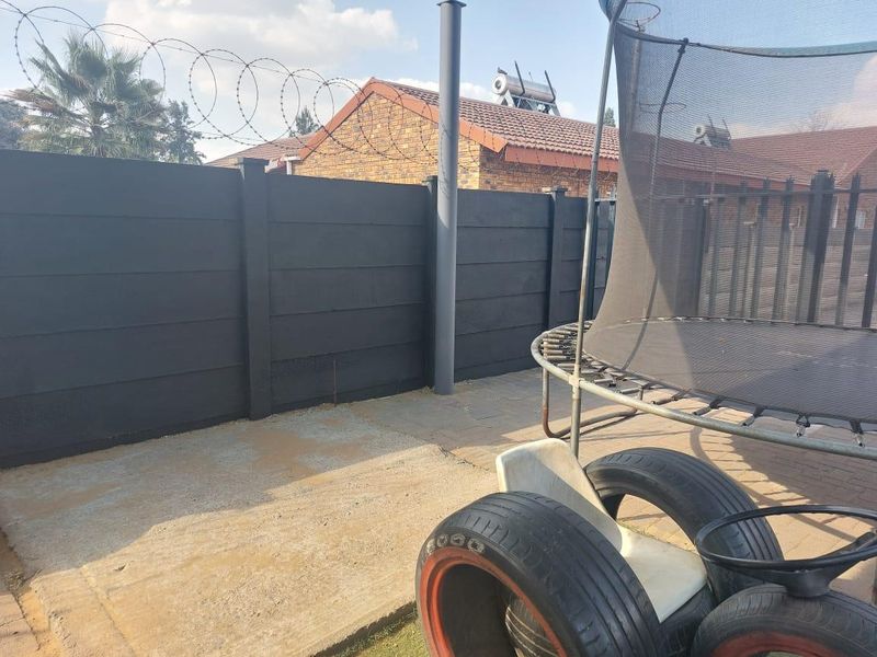 Rear outdoor area featuring a paved patio, enclosed by a precast concrete boundary wall topped with security razor wire.