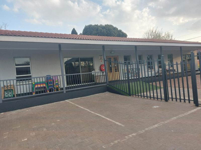 Front exterior view of an industrial or commercial property featuring a paved driveway, covered walkway, and secure steel fencing.
