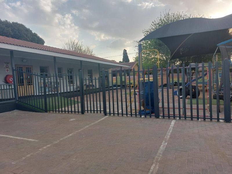 Exterior view of the property featuring a paved parking area, secure steel fencing, and a covered outdoor play space with a shade sail.