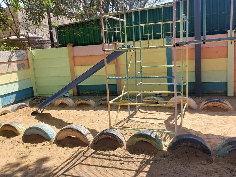 Outdoor play area featuring a sand pit, metal climbing frame, slide, and a painted precast concrete boundary wall.