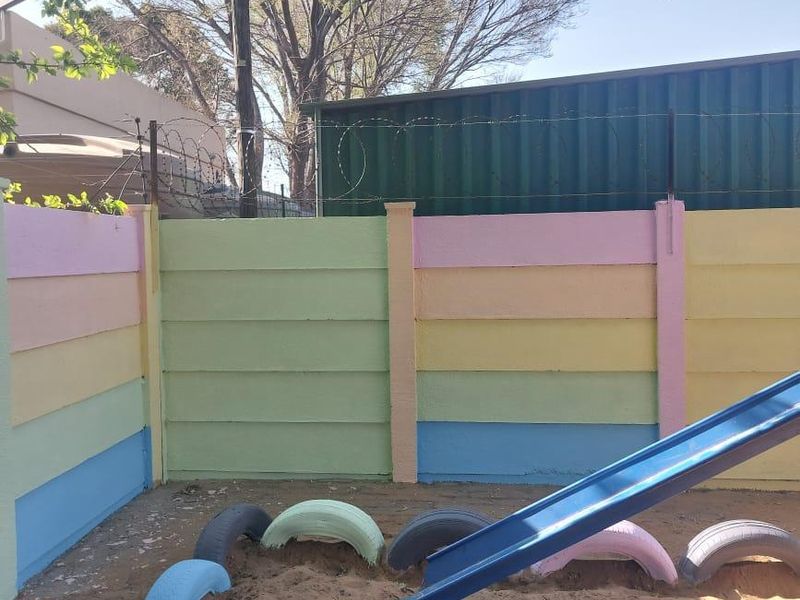 Outdoor play area featuring a sand pit enclosed by a multi-colored precast concrete boundary wall with security razor wire.