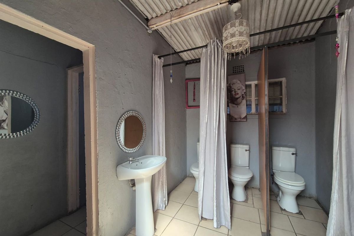A functional commercial restroom facility featuring multiple toilets with privacy curtains, a pedestal basin, and tiled flooring under an exposed corrugated metal roof.