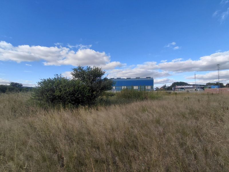 A view of the vacant commercial land featuring natural grass coverage with surrounding industrial buildings in the background.