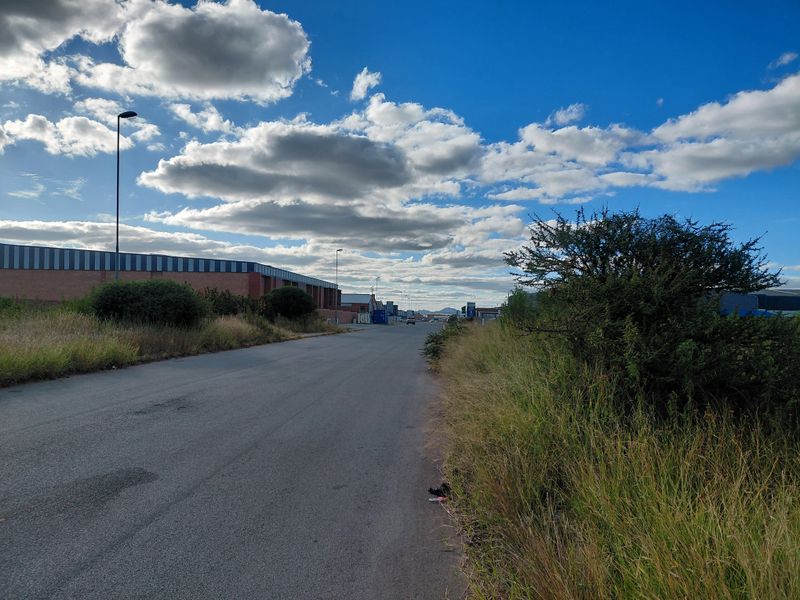 A view of the street frontage showing the access road, adjacent commercial warehouse structures, and surrounding landscape in a commercial area.